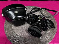 Nikon EM camera and black leather Nikon case, case shows wear with a scuffed spot on the front.