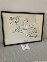 Framed black and white Picasso print showing woman sleeping, in black frame on white wall with auction lot number below.