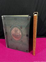 Two vintage books viewed upright, showing cover and spine. 'VANISHED TOWERS AND CHIMES OF FLANDERS' on left with textured dark cloth cover and gold title, and 'THE WHITE ROBE' with leather spine and cloth cover on right.