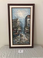 Full front view of framed vintage oil painting with Paris street scene depicting two people walking on cobblestone street near flower stands and buildings.
