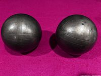 Two solid metal bocce balls with engraved lines, positioned on a magenta surface showing their shape and finish.
