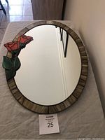 Full top-down view of the oval mirror with stained glass flower on the left side and beige/brown frame.