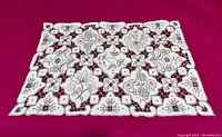 Detailed view of a placemat showing intricate floral and geometric cutwork embroidery in ecru thread on linen fabric.
