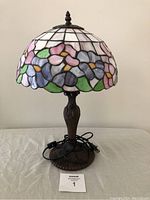 Lamp on table with unplugged cord in front showing the stained glass floral shade and bronze base