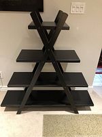 Front view of black wooden trestle shelf showing four wide rectangular tiers supported by X-shaped side frames.