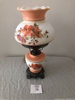 Vintage floral hurricane lamp with glass shade and base, orange-pink flower pattern, dark metal decorative base.