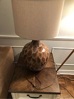 Full view of the lamp showing the bulbous lava drip ceramic base in caramel brown and beige colors topped with a beige fabric shade.