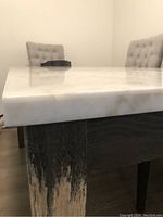 Close-up of the corner showing the white marble top with grey veining and the worn wood leg with scratching damage near the bottom.