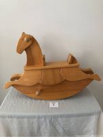Side view of child's solid wood rocking horse, showing the smooth natural wood finish and carved horse head with ear and nose details, along with rocking curved base and backrest.