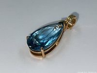 Angled view showing pear-shaped blue topaz and gold prong setting