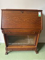 Front view of antique oak secretary desk showing drop front closed and barrister bookcase below with glass front, claw-foot legs visible.