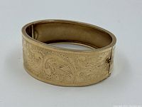 Angled view of closed bracelet showing hinge and engraved scrollwork pattern