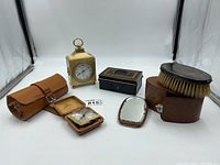 Full lot of vintage items: travel wind-up clock, small mantle clock, grooming kit, brush, comb, mirror and lockbox.