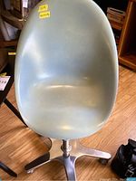 Vintage turquoise molded chair with metal swivel base and caster wheels shown from front and slightly angled views on wood floor.