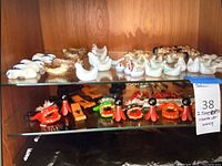 Glass cabinet shelf holding the collection of ceramic and wooden chop stick holders including hens, chickens, cats, and dragon figures.