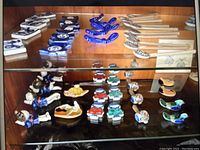 Two full shelves of assorted ceramic chopstick holders in blue, multicolor, and some brown tones arranged in glass display case