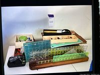 Overview of crafting tools, rulers, and beads on a table showing wooden ruler holder, box trays with beads, crafting tools, and rulers of different sizes.