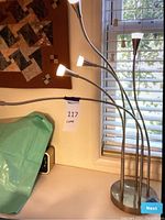 Full view of the desk lamp on a desk near a window, showing five flexible necks with cone-shaped LED lights turned on.