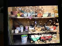 Front view of wooden shelving with ceramic pots of various sizes and colors, gardening buckets and plastic garden wagons underneath.