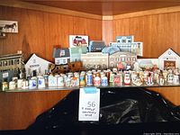 Wide-angle view of the collection showing rows of assorted decorative thimbles in front of an array of wooden landmark building models on a shelf.