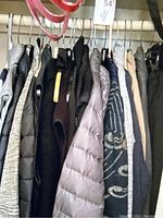 Multiple jackets and coats hanging on a rack including a grey puffer jacket, dark coats, and other outerwear.
