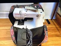 Front view of white Janome Jem Gold sewing machine in floral carry bag with foot pedal in foreground