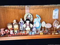Wide view of shelf containing various Japanese and English decorative figurines, dolls, miniatures, and ornamental eggs.