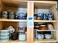 Two shelves of Japanese ceramic cups, bowls, and plates showing a wide assortment of floral and textured designs.