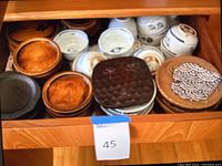 Drawer with assortment of wooden plates and ceramic cups and bowls, showing textures and carved patterns on wooden items alongside painted ceramic pieces.