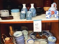 Shelf display of various Japanese ceramic cups, plates, sake bottles, and bowls in blue and white patterns along with wooden items.