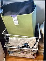 Large green storage bin filled with layered fabric pieces and two wire baskets below containing white and other fabric pieces. Image shows storage and volume of fabric pieces.