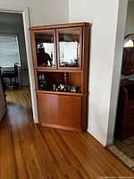 Mid century corner china cabinet hutch positioned in a corner with glass upper cabinet doors and wooden lower cabinet doors.