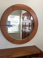 Front view of the round wooden framed mirror showing mid-century style segmentation and mirror reflection.