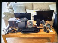 Wide shot of lot on wooden table showing all items: monitors, speakers, media players, phones, game, cables
