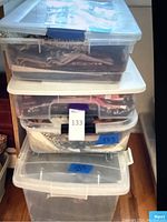 Stack of four clear plastic containers filled with fabric swatches and sewing materials, lids closed and labeled