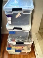 Four stacked clear plastic storage bins holding various pieces of fabric and sewing materials, showing the exterior storage containers.