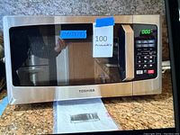 Front view of Toshiba microwave on countertop with label showing dimensions 11x13x19 and note '100 microwave'