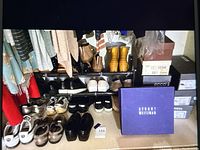Wide view of shoes on rack and floor showing multiple pairs and brands including Stuart Weitzman boots box, Ecco, Cole Haan, Puma sneakers, sandals and black heels mostly in sizes 6 to 7.