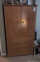 Wooden armoire front closed, showing two doors and three drawers with wooden knobs.