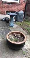 Photo shows the blue-green resin 2-piece bird bath, large round planter filled with soil and dried plants, and additional smaller black plant pots.