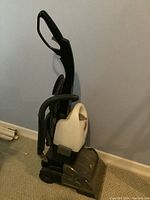 Front and side view of the black and white upright cleaner showing the overall structure, water tank, and handle.