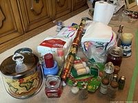 Full view of the ice bucket, candles, salt and pepper shakers, napkins, and wrapping paper arranged together on a surface with wooden cabinet background.