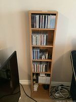 Full view of wooden CD stand filled with CDs, cassettes and two small statuettes on middle shelf