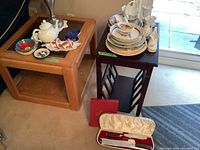 Overview of teapot, small dishes and bowls on wooden side table, adjacent table with stacked plates, vases, and faux bone carving set case