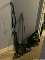 Photo of Bissell upright vacuum cleaner, carpet cleaner, stick vacuum, broom, and floor cleaner grouped leaning against wall.