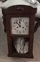 Front view of vintage wood cased wall clock showing white dial with black Arabic numerals and black hands.