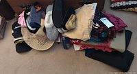 Top view of assortment of clothing items, slippers, straw hat, and scarves laid out on carpet.