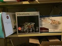 Photo showing three boxed sets: Vibrations 7-piece salad set, CorningWare French White oval casserole, and unopened boxes for Dot glasses