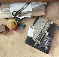 Photo showing metal shears, various rulers, Boston hole punch, mineral dictionary, pin cushion, and eraser on the floor.