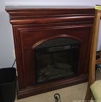 Front view of the electric fireplace showing full unit with wooden surround and black control panel, realistic faux logs visible inside glass.